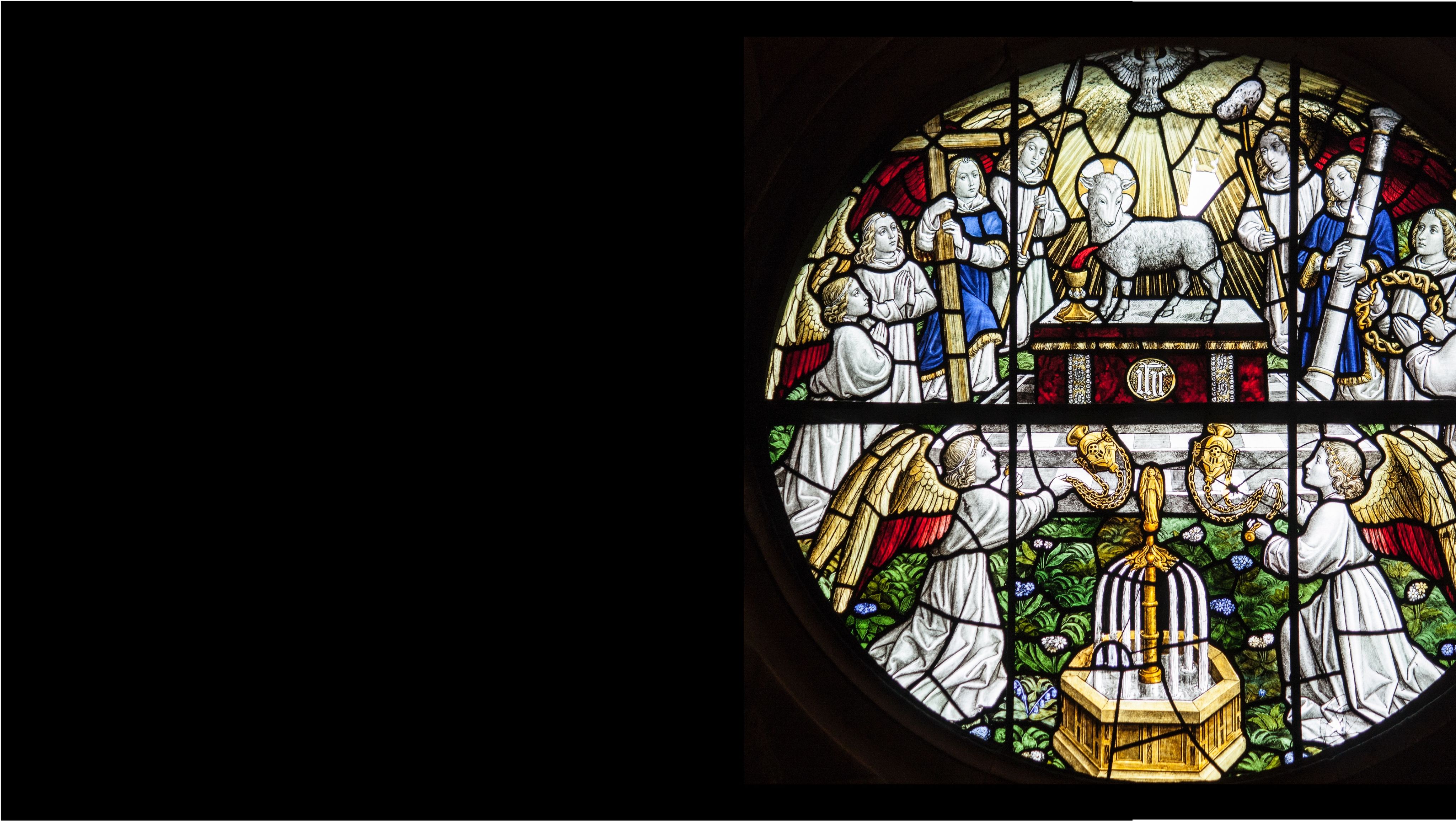 Detail from a window in the church of St Philip & St James in Oxford. Showing a lamb on an Alter surrounded by Angels bearing gifts. Image is brightly coloured in blues and gold..