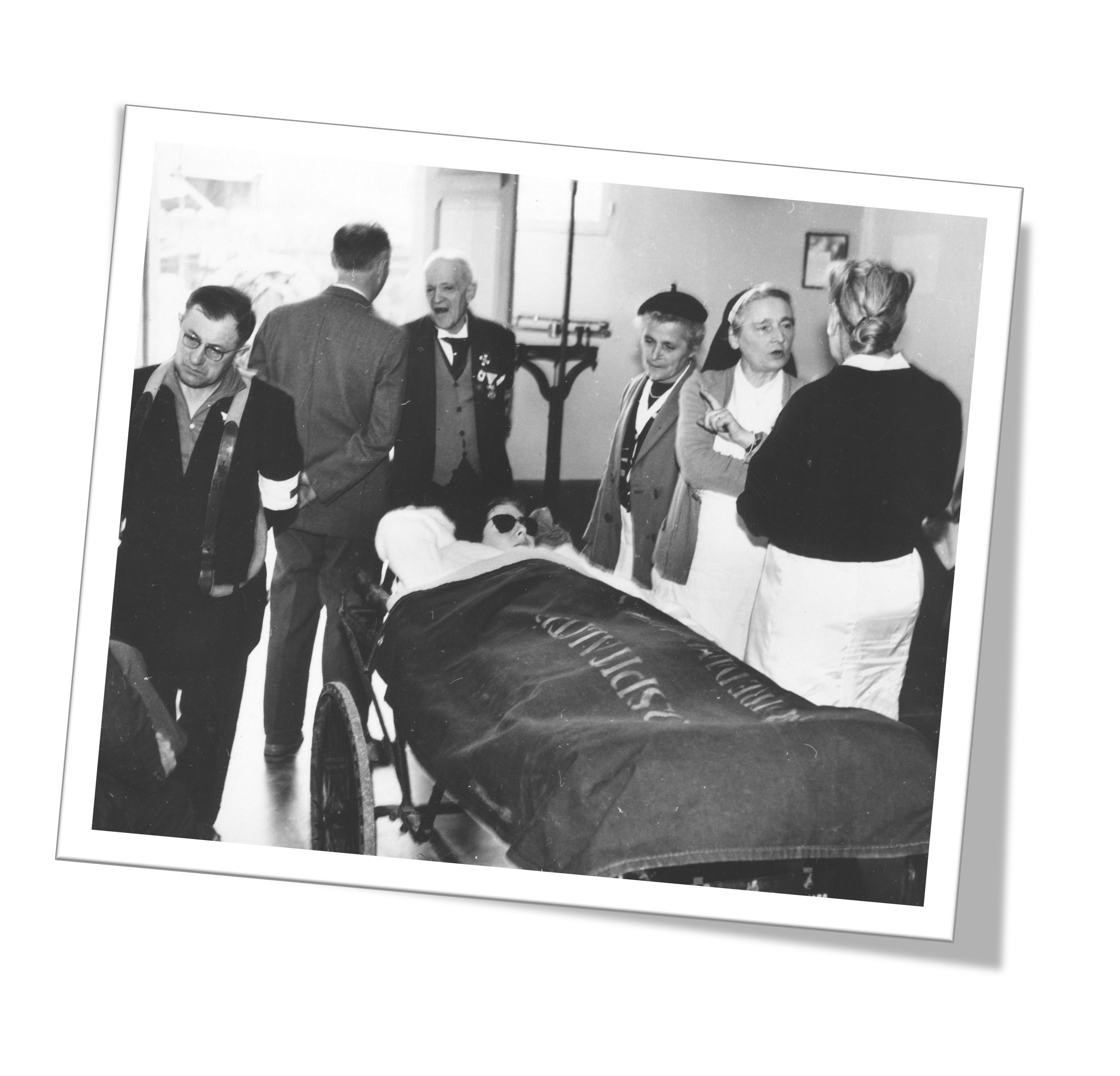 Photograph depicts doctors surrounding a patient. Medical staff are members of the Lourdes Medican Bureau. The images is in black & white and dates from around 1950.