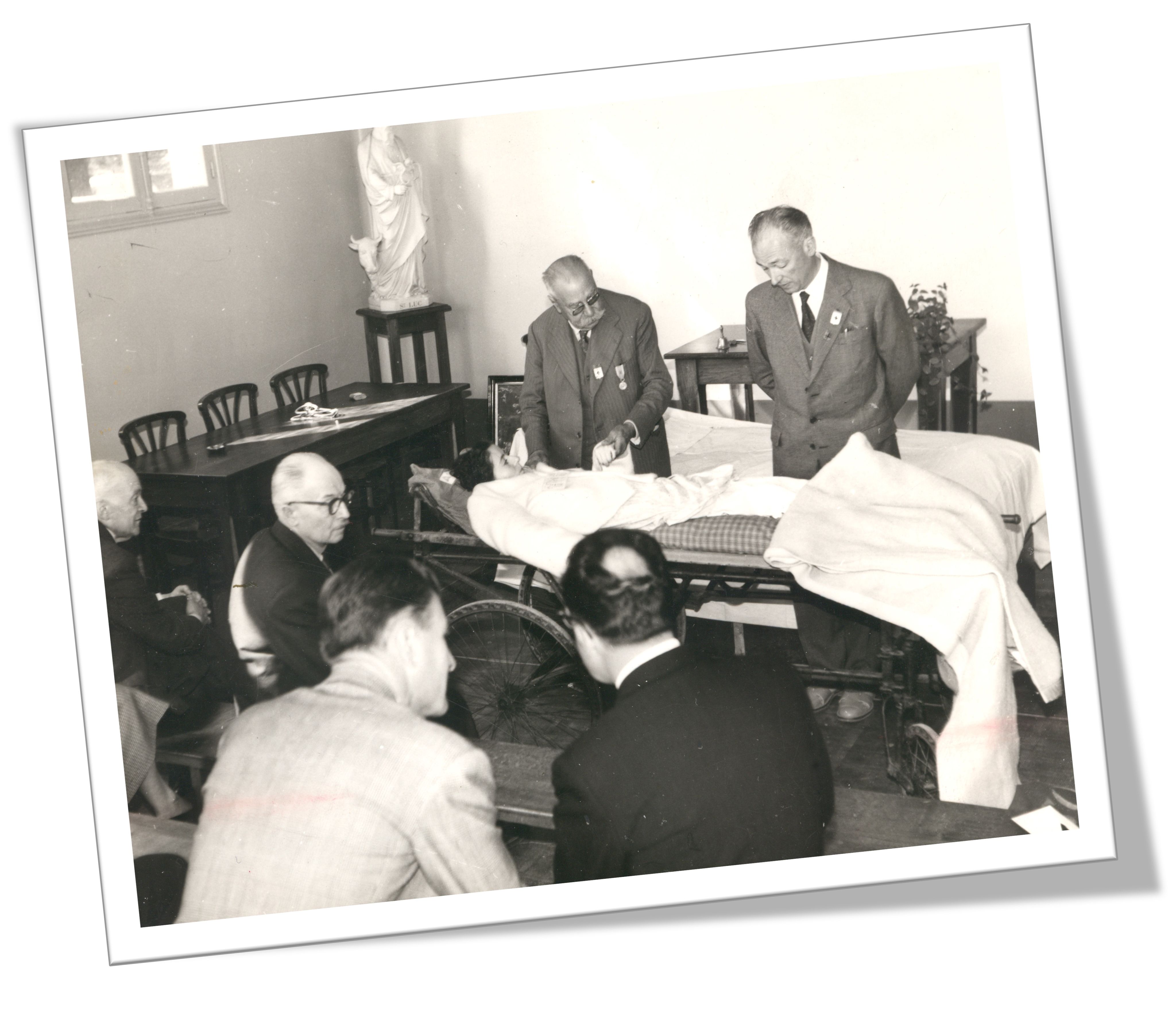 Photograph shows doctors attending to a patient. Doctors are members of the Lourdes Medical Bureau. The photograph is in black & white and dates from around 1950